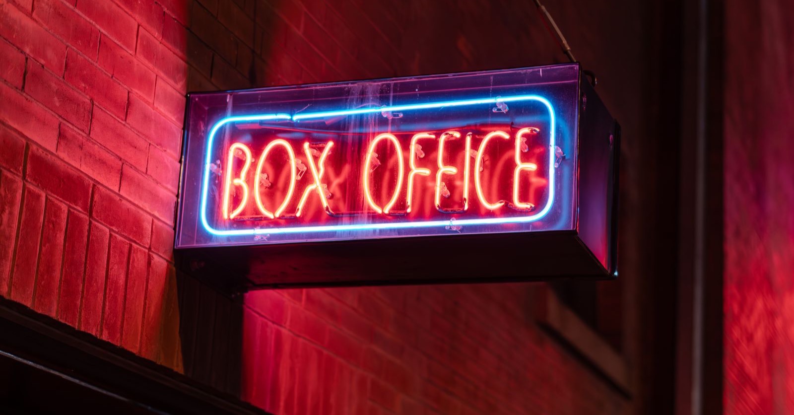 A red and blue neon box office sign on a brick wall at night