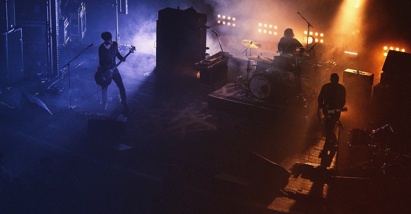 A three piece band playing on a smoky stage under blue and orange lights, seen from above
