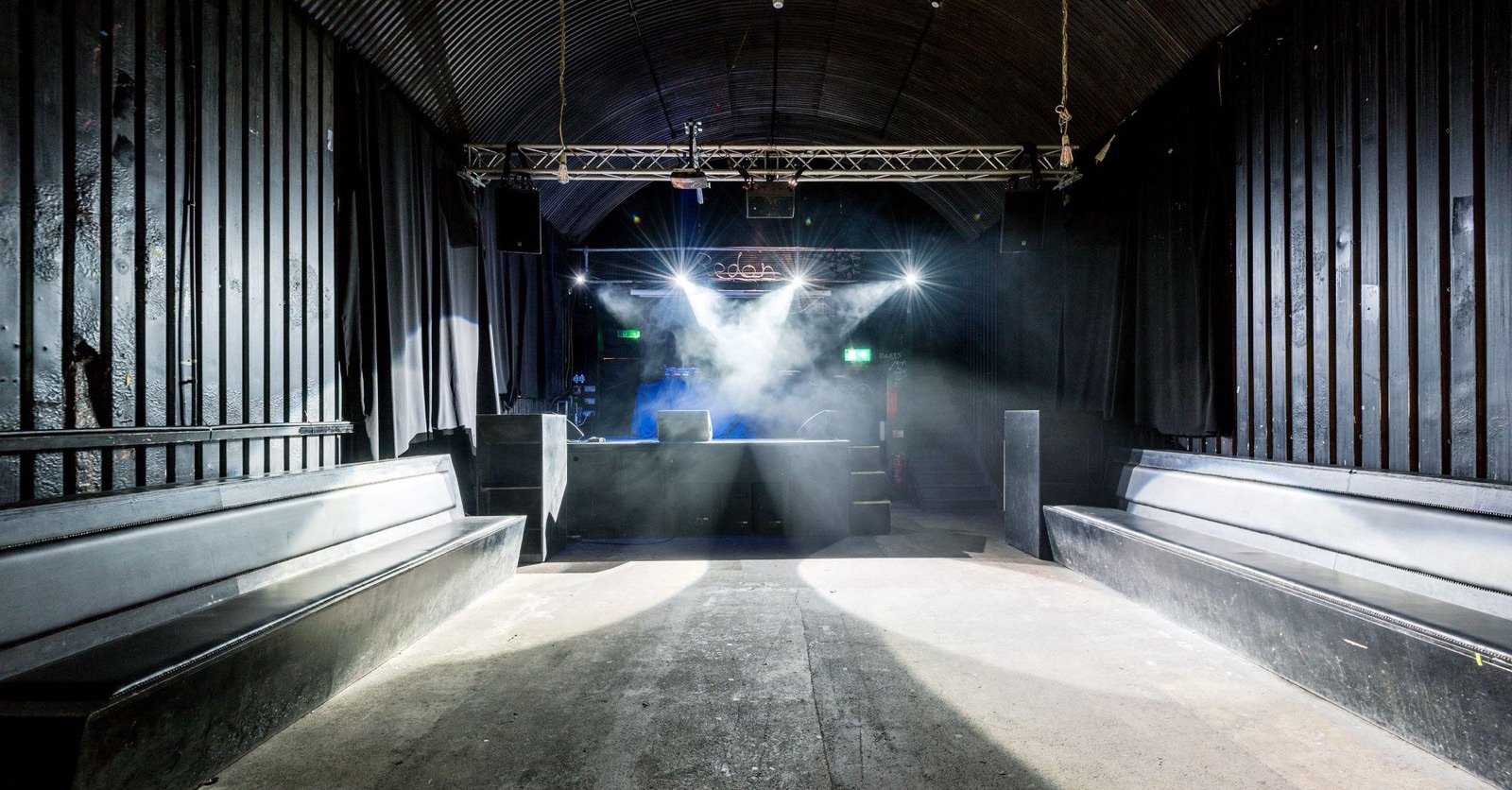 An empty club room under an arched roof, with the stage lights and haze on and nobody on the dancefloor