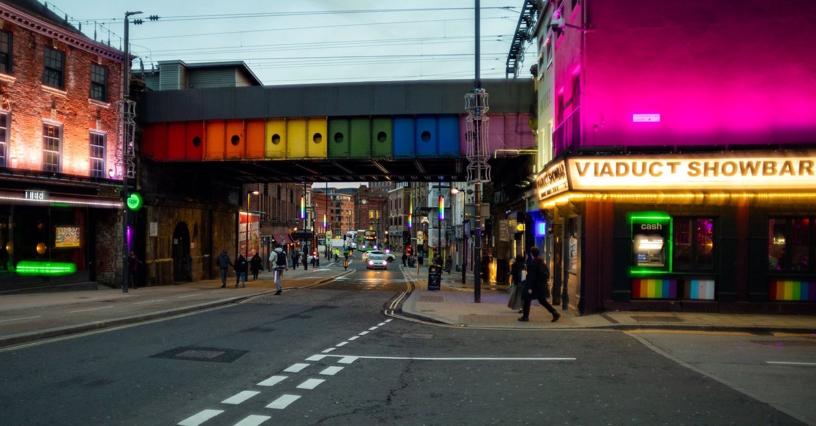 A Leeds street at dusk with venue lights already on and a few people walking