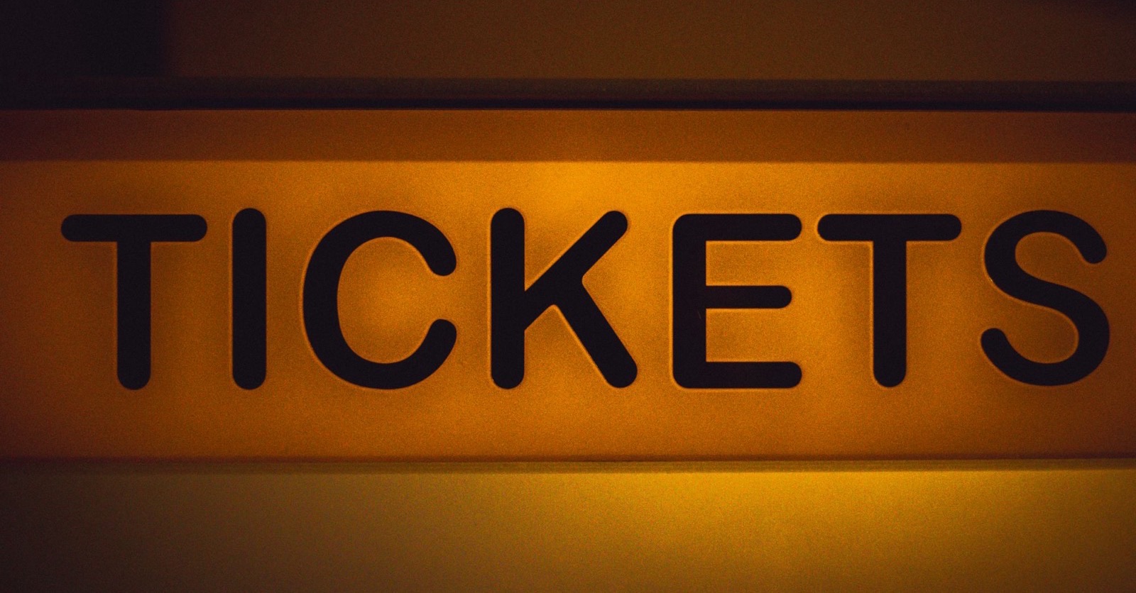 A lit yellow sign reading TICKETS against a dark wall