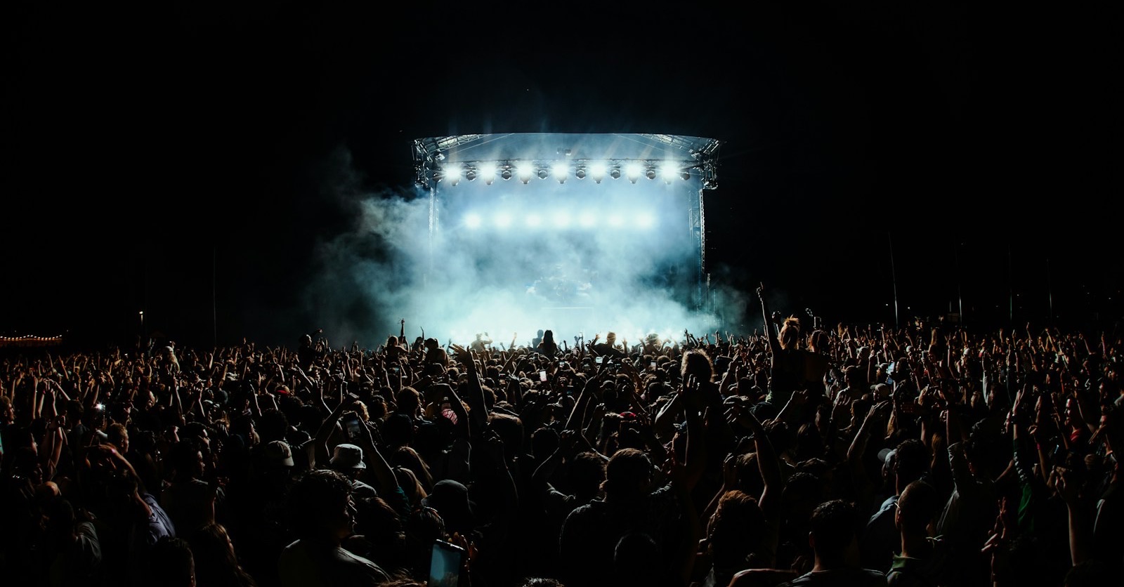 A crowd with hands raised in front of a lit festival stage at night